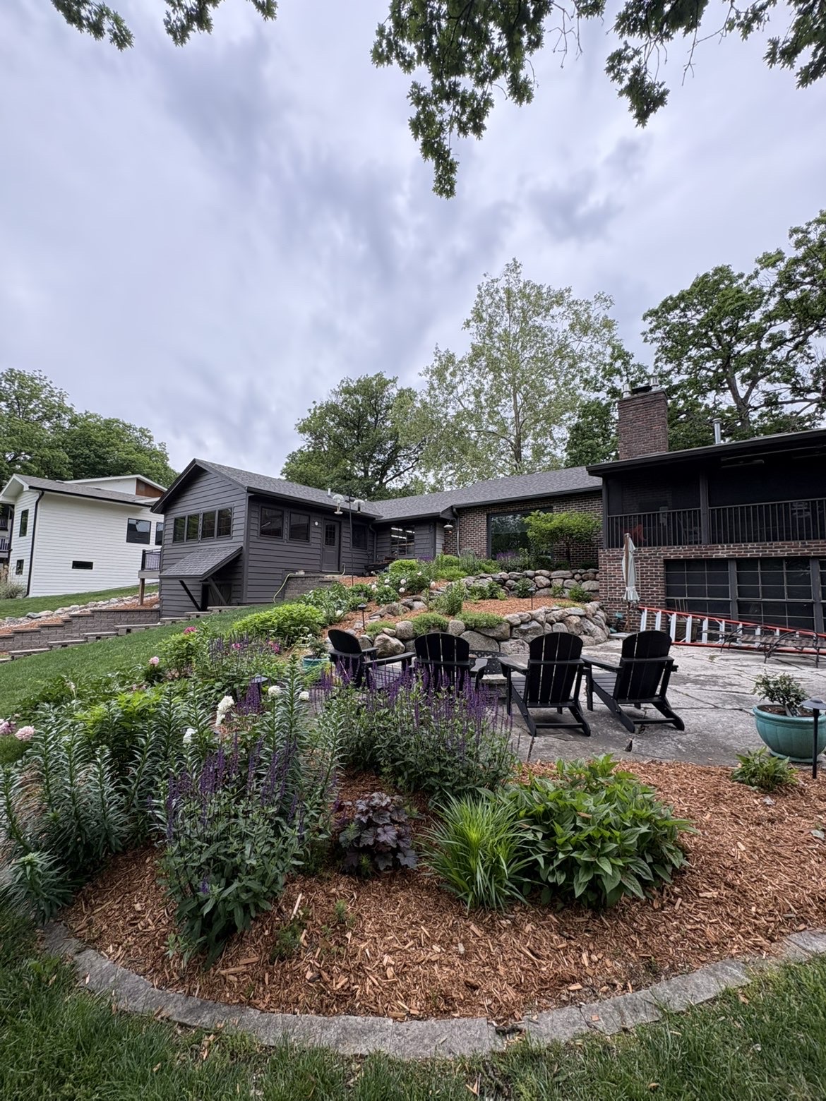 Backyard landscape design with boulder retaining wall, perennial gardens, mulched beds, and patio seating area in Des Moines, Iowa